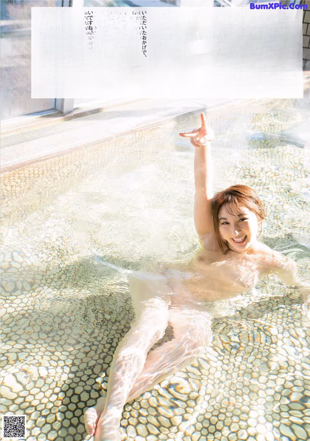 A naked woman in a swimming pool with her arms outstretched.