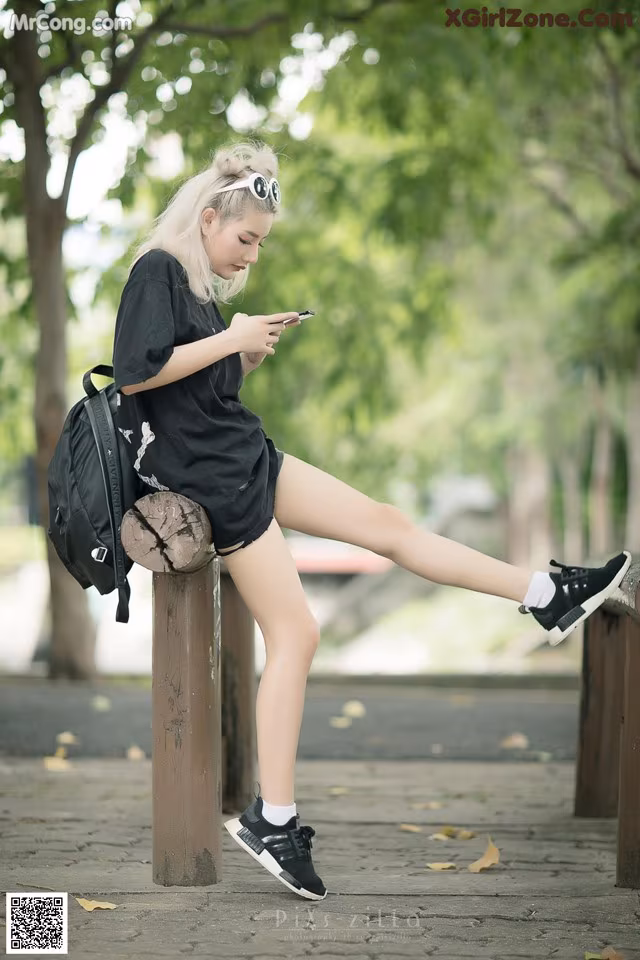 A woman sitting on top of a wooden post looking at her phone.