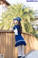 A woman in a blue and white uniform leaning against a fence.