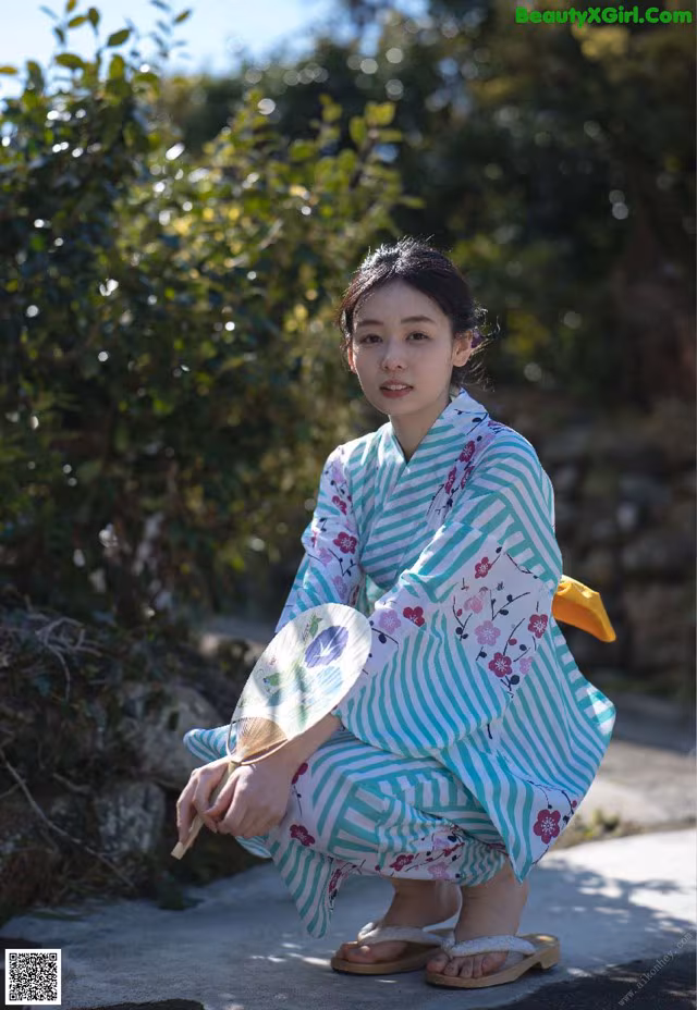 A woman in a kimono crouching down with a fan.