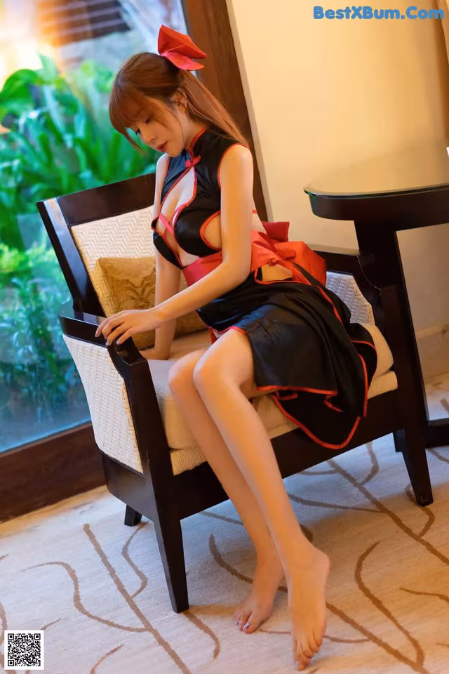 A woman in a black and red dress sitting on a chair.