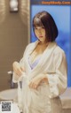 A woman in a white robe standing in a bathroom.