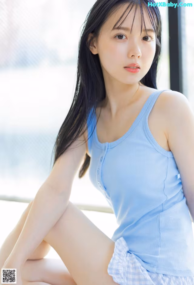 A woman in a blue tank top sitting on a window sill.