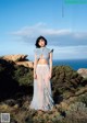 A woman standing on top of a hill next to the ocean.