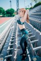 A woman in a sports bra top and leggings standing in a stadium.