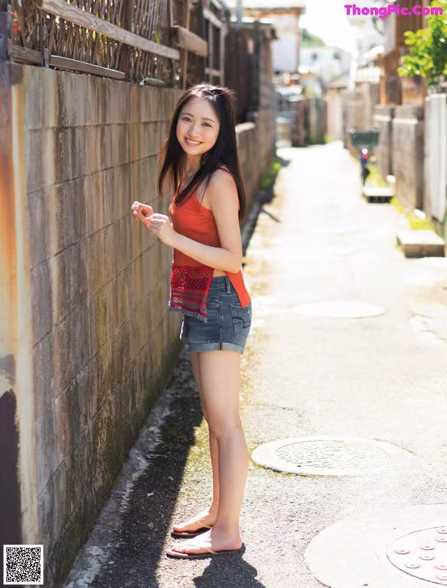 A young woman standing on a sidewalk next to a wall.