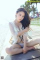 A woman sitting on a wooden bench on the beach.