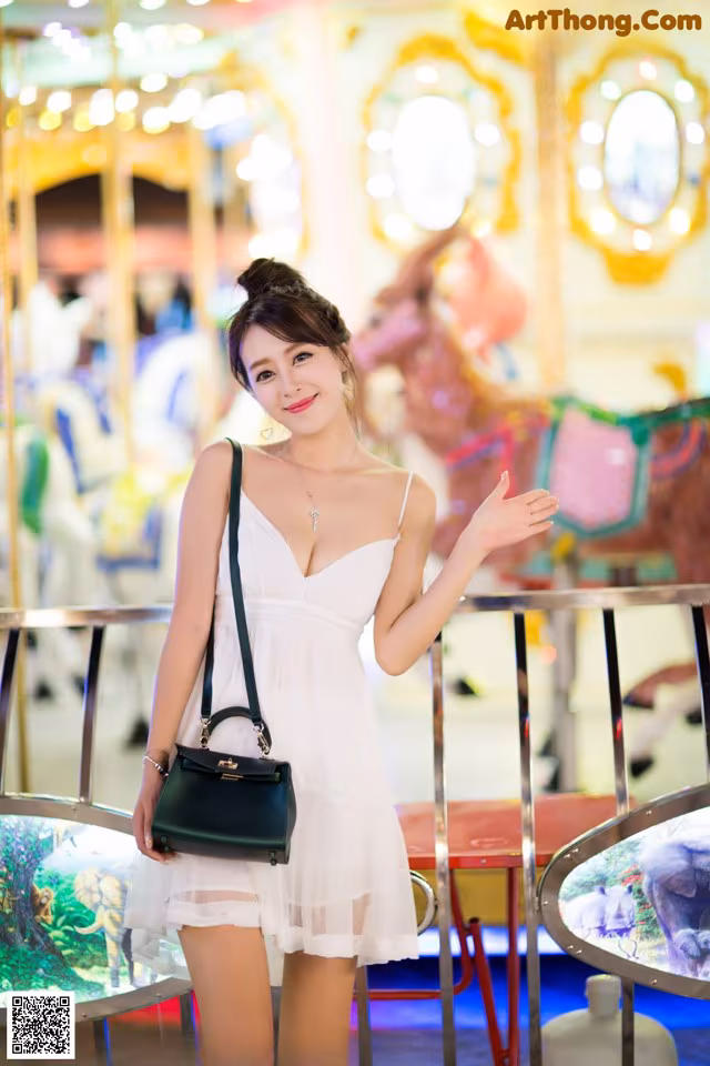 A woman in a white dress standing in front of a carousel.