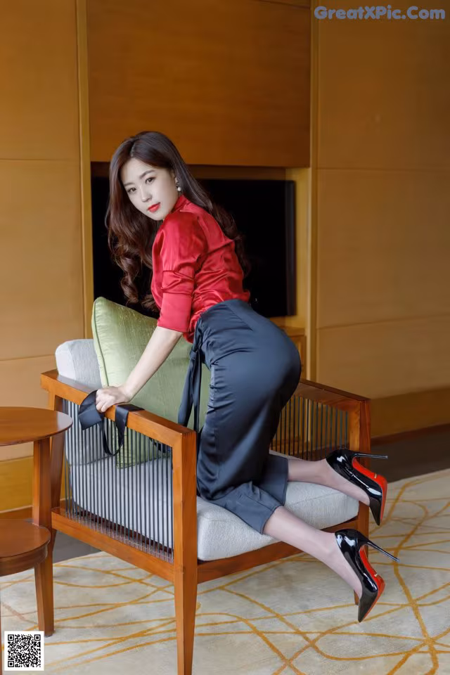 A woman in a red shirt and black skirt sitting on a chair.
